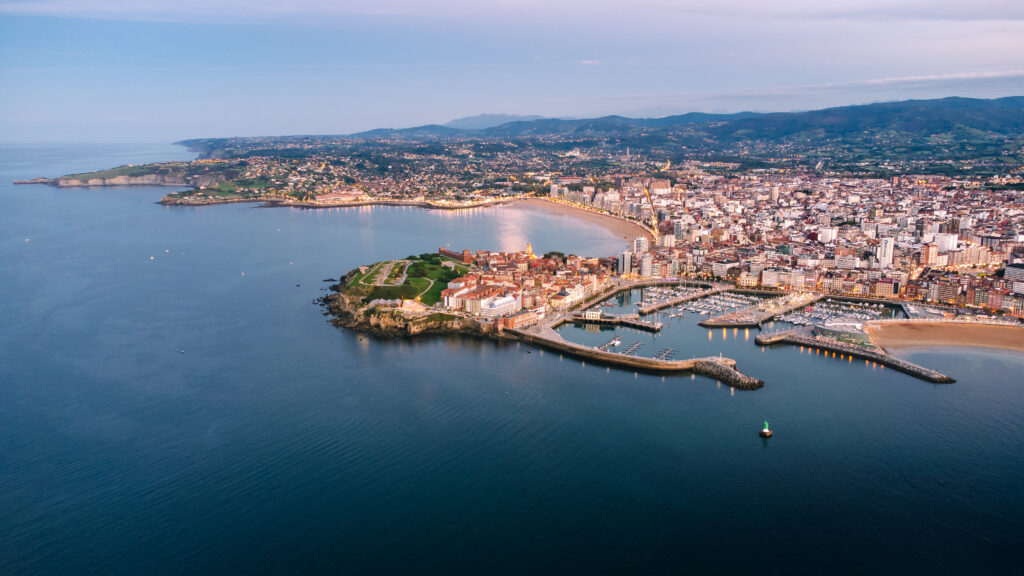 Aerial footage of gijon cityscape ocean beach harbor and urban skyline illuminated at dusk after sunset